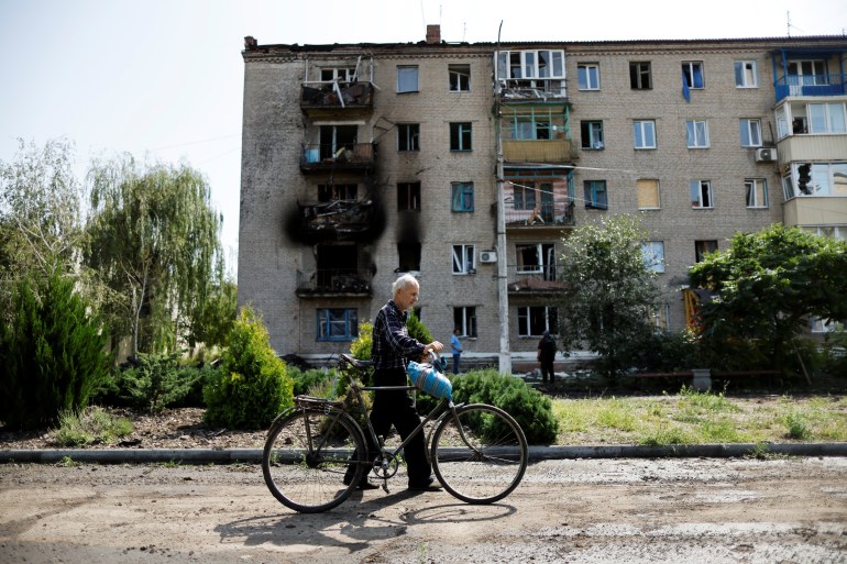 A Ukrainian man walks with his bicycle in front of damaged houses following recent Russian shelling in Slovyansk.