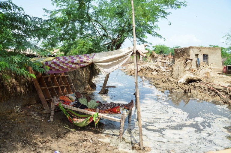 A man rests on a cot made with tope amid flood waters infront of his damaged house following rains and floods during the monsoon season in Jafarabad, Pakistan August 28, 2022