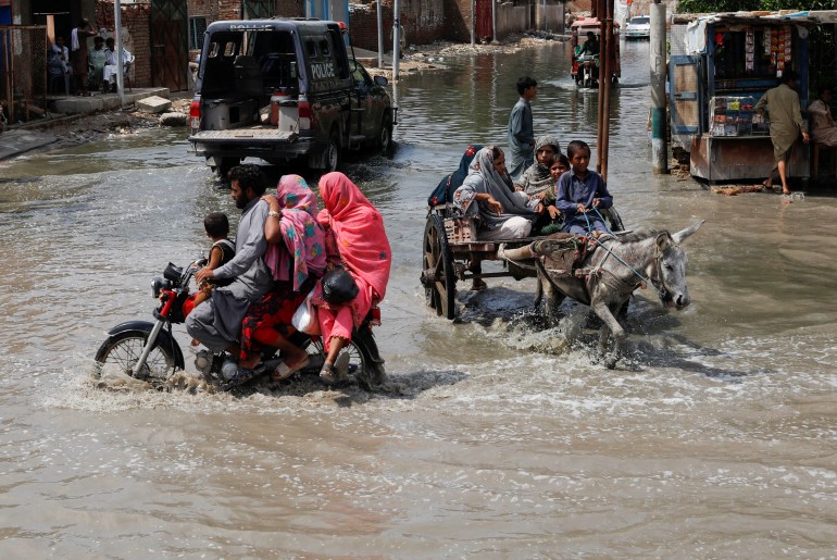 Families travel through water-filled streets on motorcycle and on a donkey cart in Jacobabad, Pakistan.