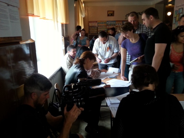 A separatist 'observer' in a black T-shirt next to election officials at the Donetsk 'referendum'