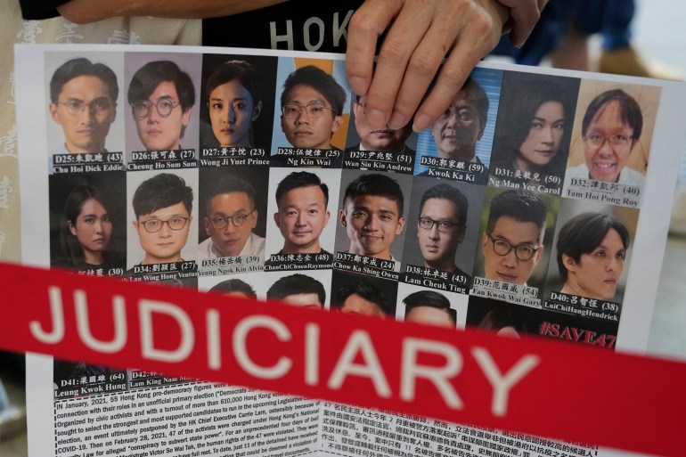一名站在香港法院外的人举着一张海报，上面展示了 47 名民主政客和活动人士因组织初选而被捕，以选择自己的候选人参加选举，该选举随后被推迟