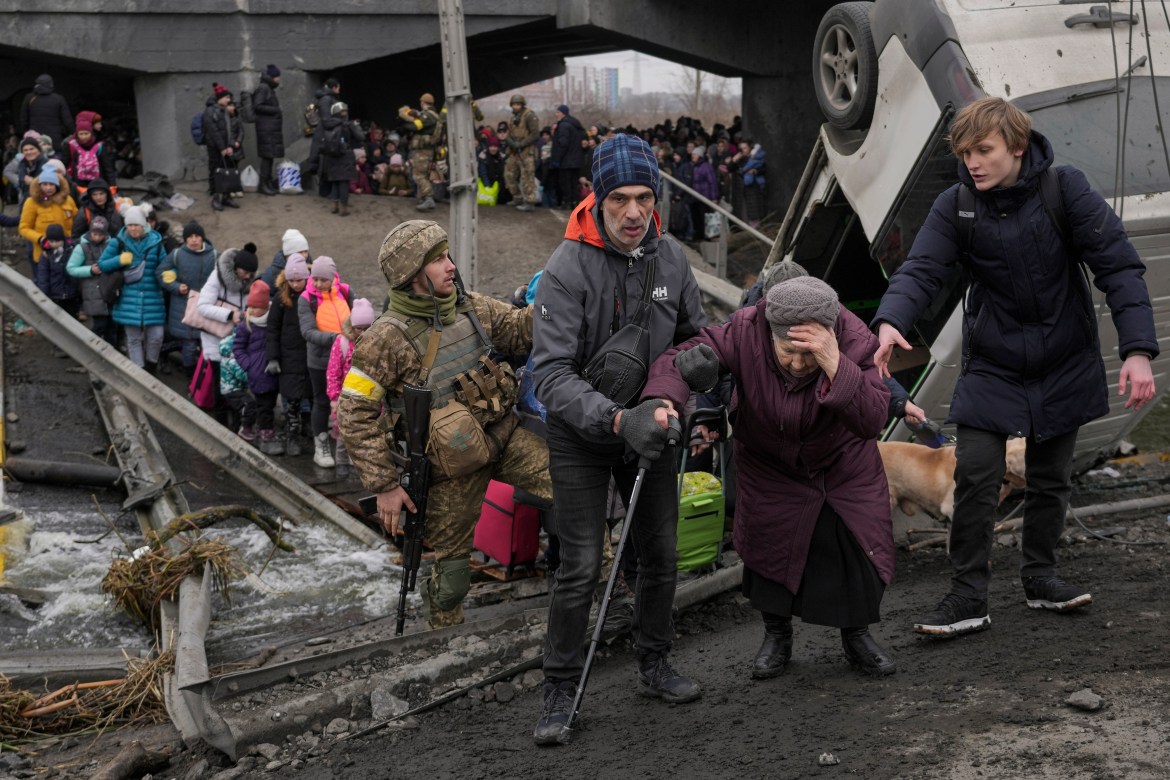 An elderly lady is assisted to cross the Irpin river on an improvised path under a bridge, that was destroyed by Ukrainian troops designed to slow any Russian military advance, while fleeing the town of Irpin, Ukraine