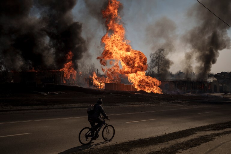 A man rides his bike past flames and smoke rising from a fire following a Russian attack in Kharkiv, Ukraine