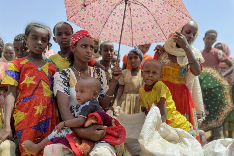 Women and children wait under the shade of an umbrella at a food distribution site in the town of Adi Mehameday, in the western Tigray region of Ethiopia