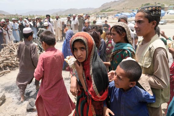 A young Afghan girl stands amid children and adults waiting to receive aid at a camp