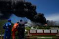 Workers of the Cuba Oil Union, known by the Spanish acronym CUPET, watch a huge rising plume of smoke from the Matanzas Supertanker Base, as firefighters work to quell a blaze which began during a thunderstorm the night before, in Matazanas, Cuba