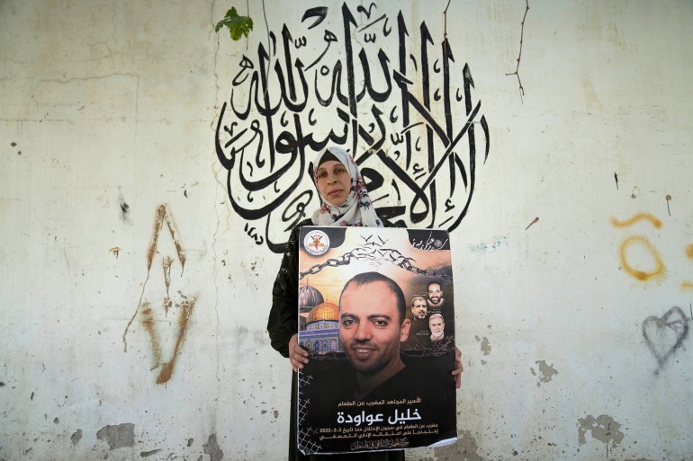 Palestinian Dalal Awawdeh poses with a poster of her husband Khalil Awawdeh, who is a prisoner in Israel, at the family house, in the West Bank village of Idna, Hebron, Tuesday, Aug. 9, 2022. Awawdeh, who is on a protracted hunger strike, was moved Thursday from an Israeli jail to a hospital because of his worsening condition, the prisoner’s wife said. Arabic in the background reads "There is no God but Allah, Muhammad is the Messenger of Allah." (AP Photo/Nasser Nasser)