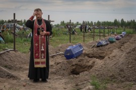 A priest on Thursday prays for unidentified civilians killed in Bucha, on the outskirts of Kyiv. Their bodies were found after Russian forces left the area more than a month after invading Ukraine [Efrem Lukatsky/AP Photo]