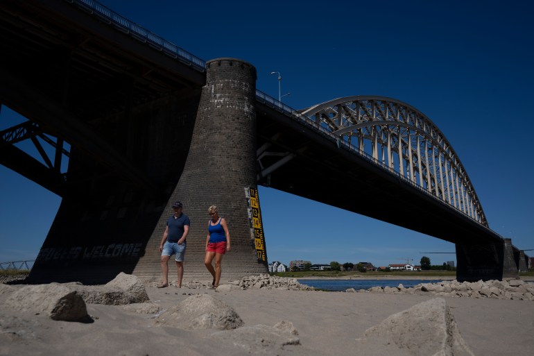 FILE - People take a stroll on the river bed of the Waal as water levels dropped because of drought in Nijmegen, Netherlands, Tuesday, Aug. 9, 2022. In parts of the country a ban on daytime irrigation of agricultural land has been issued because of extreme drought. (AP Photo/Peter Dejong, File)