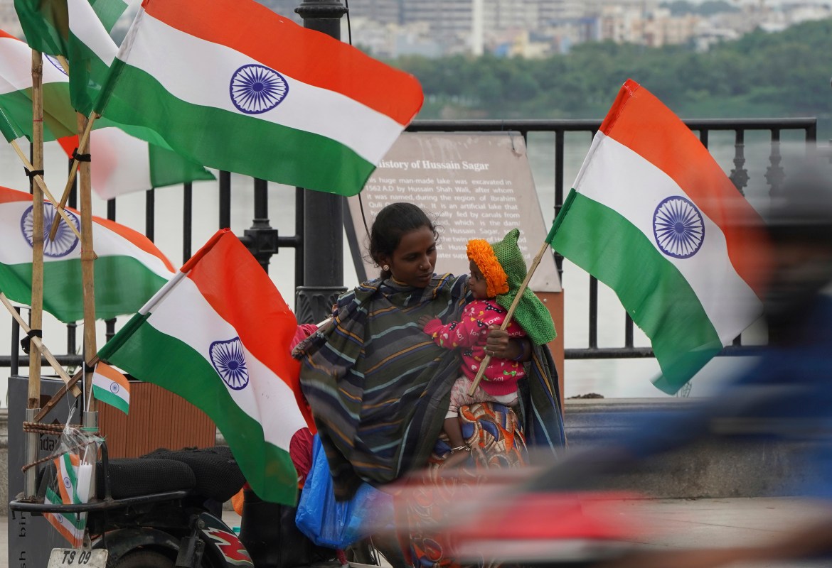 A roadside vendor carrying a child sells Indian flags