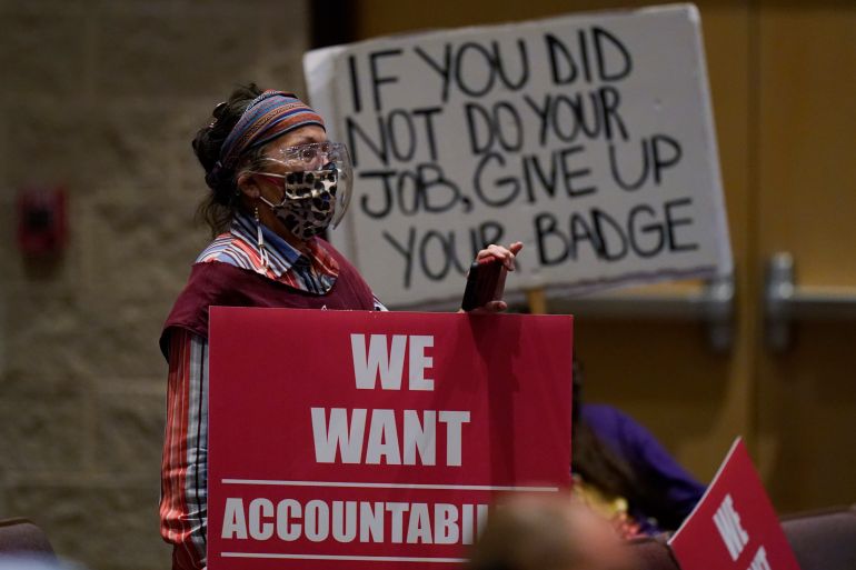 Woman wearing mask, holding red sign that says 'We want accountability'. Behind here, a large sign says 'If you did not do your job, give up your badge'.