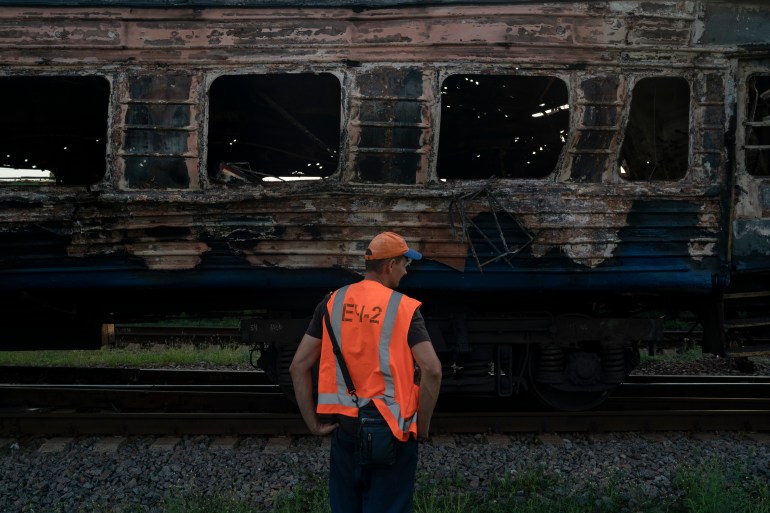 A railway worker stands next to heavily damaged train after a Russian attack on a train station Wednesday during Ukraine's Independence Day in the village Chaplyne, Ukraine,