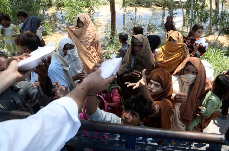 Displaced families receive food and take refuge on a roadside in Peshawar.
