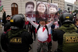 An opponent of the government of President Pedro Castillo holds photos of Castillo, his sister-in-law Yenifer and his wife Lilia Paredes with text that reads in Spanish, "Criminals".