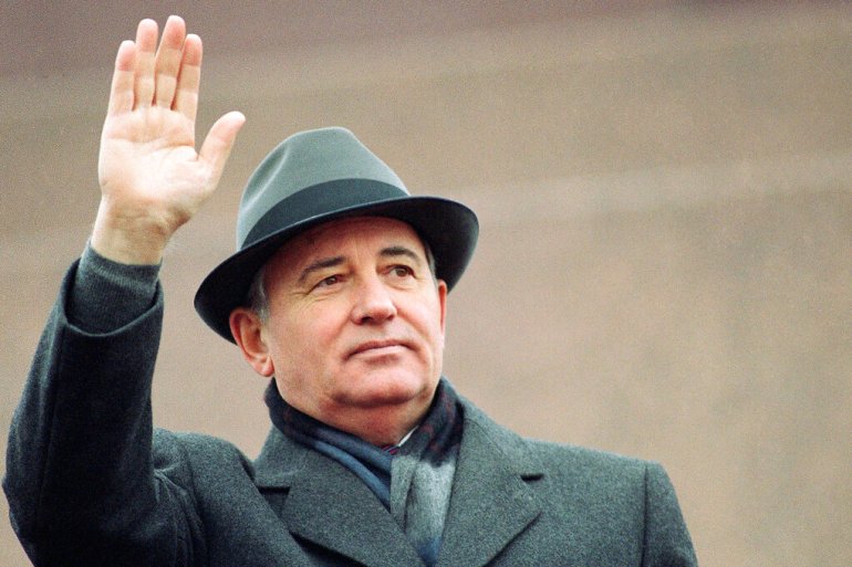 Mikhail Gorbachev in grey hat and coat waves to a crowd in 1989