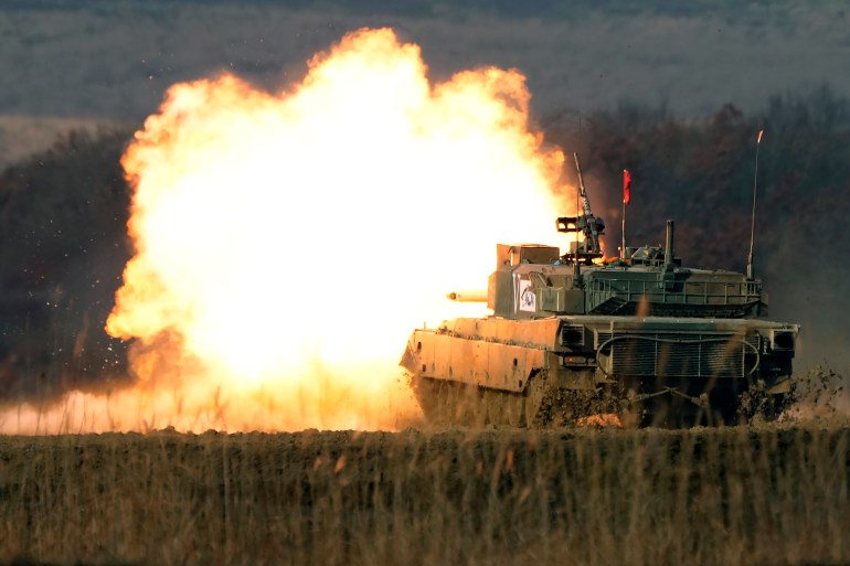 Bir Japon tankı, silahını ateşleyerek, tatbikatlar sırasında turuncu alev ve dumandan oluşan bir top oluşturuyor. 
