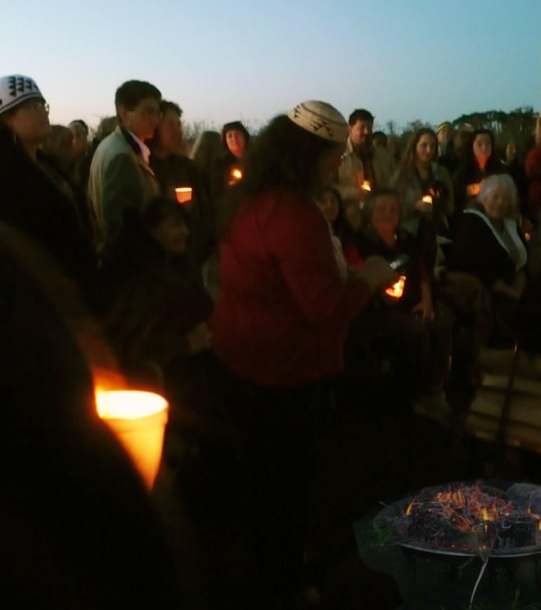 A photo of Wiyot elders, tribal members and people holding candles around a firepit at a vigil.