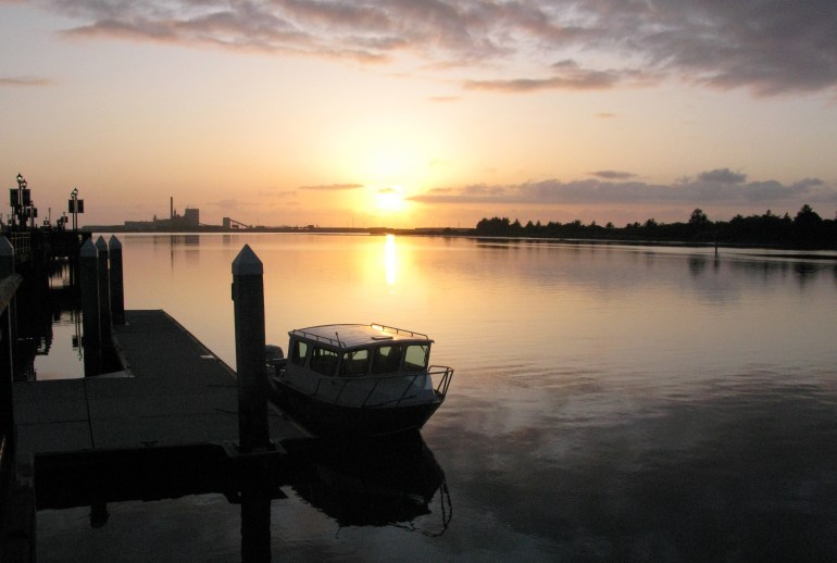 A photo of Humboldt Bay with a boat in the water and a sunset in the background.
