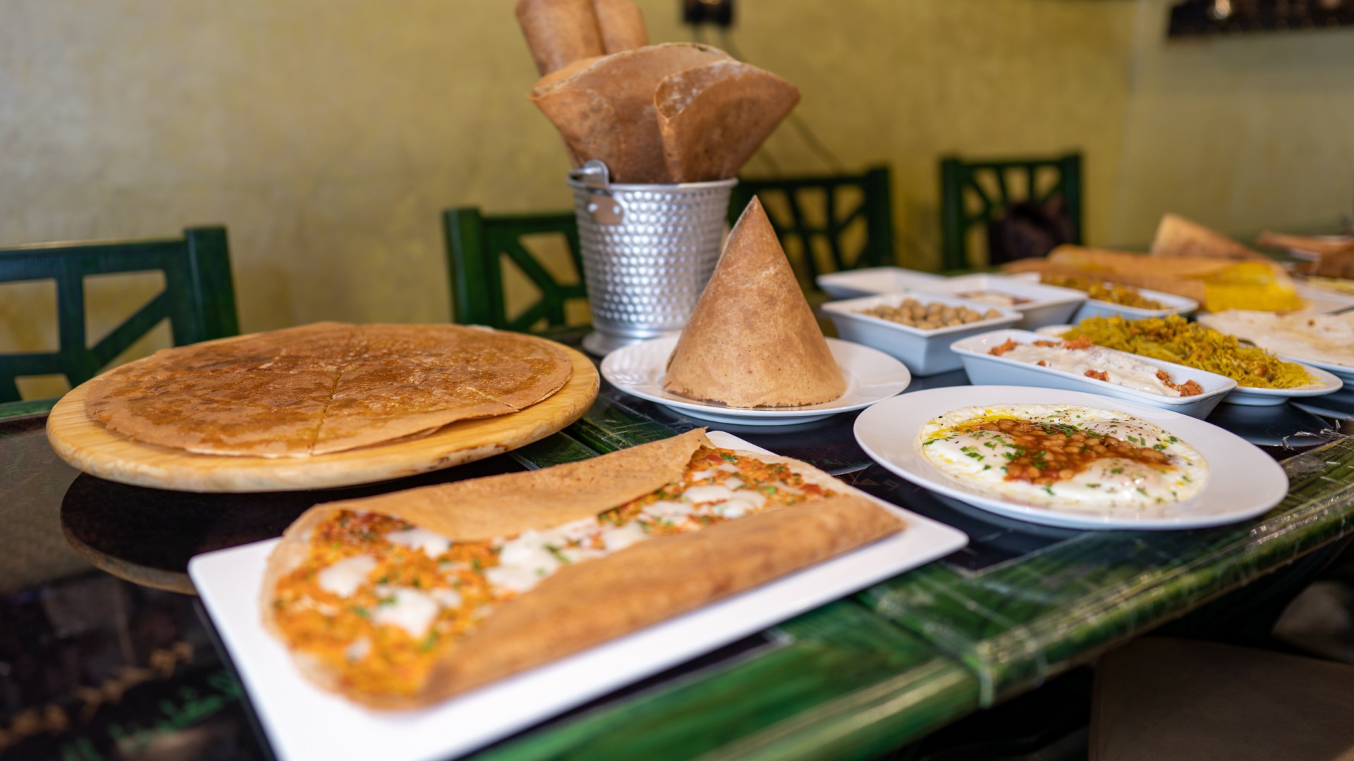 Photo of a green table full of breakfast dishes, regag breads with fillings and without, folded into fanciful shapes