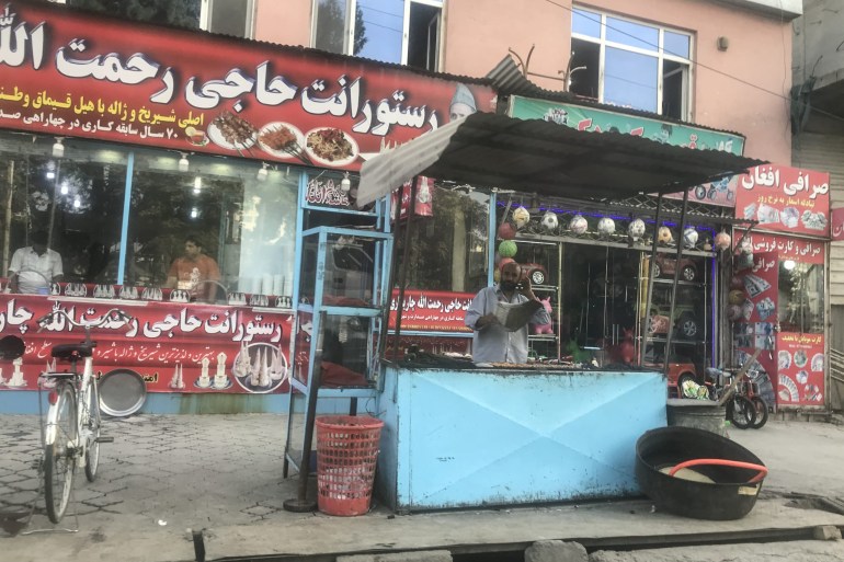 A kebab seller stands at his sidewalk stand, fanning coals