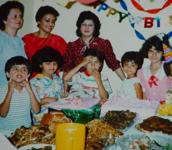 A photo from the 1980s shows three women with a group of children gathered around a table laden with kebab and naan