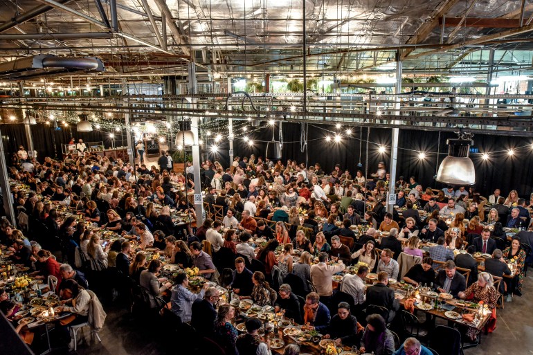 An overview of a big hall with hundreds of people seated at long tables sharing an Afghan meal