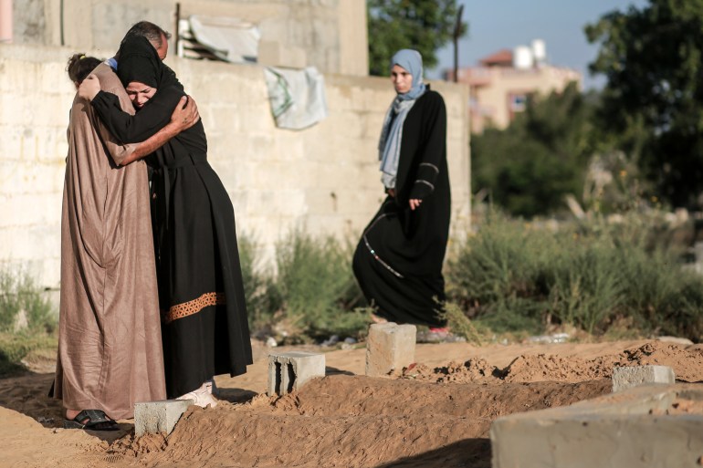 A woman hugs a man in front of a grave in Gaza