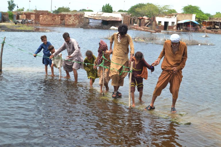 People wade through a flooded area following heavy rain in Sanghar district in Sindh province