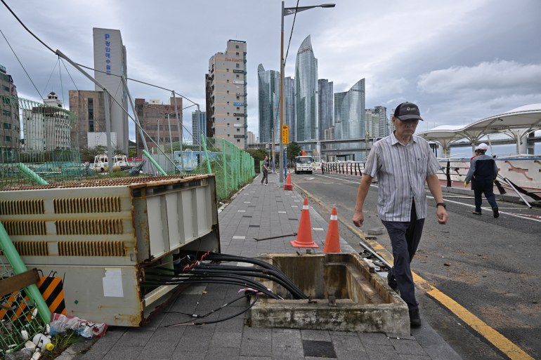A man in Busan walks past an electrical box flipped onto its side with the cables exposed by a typhoon.