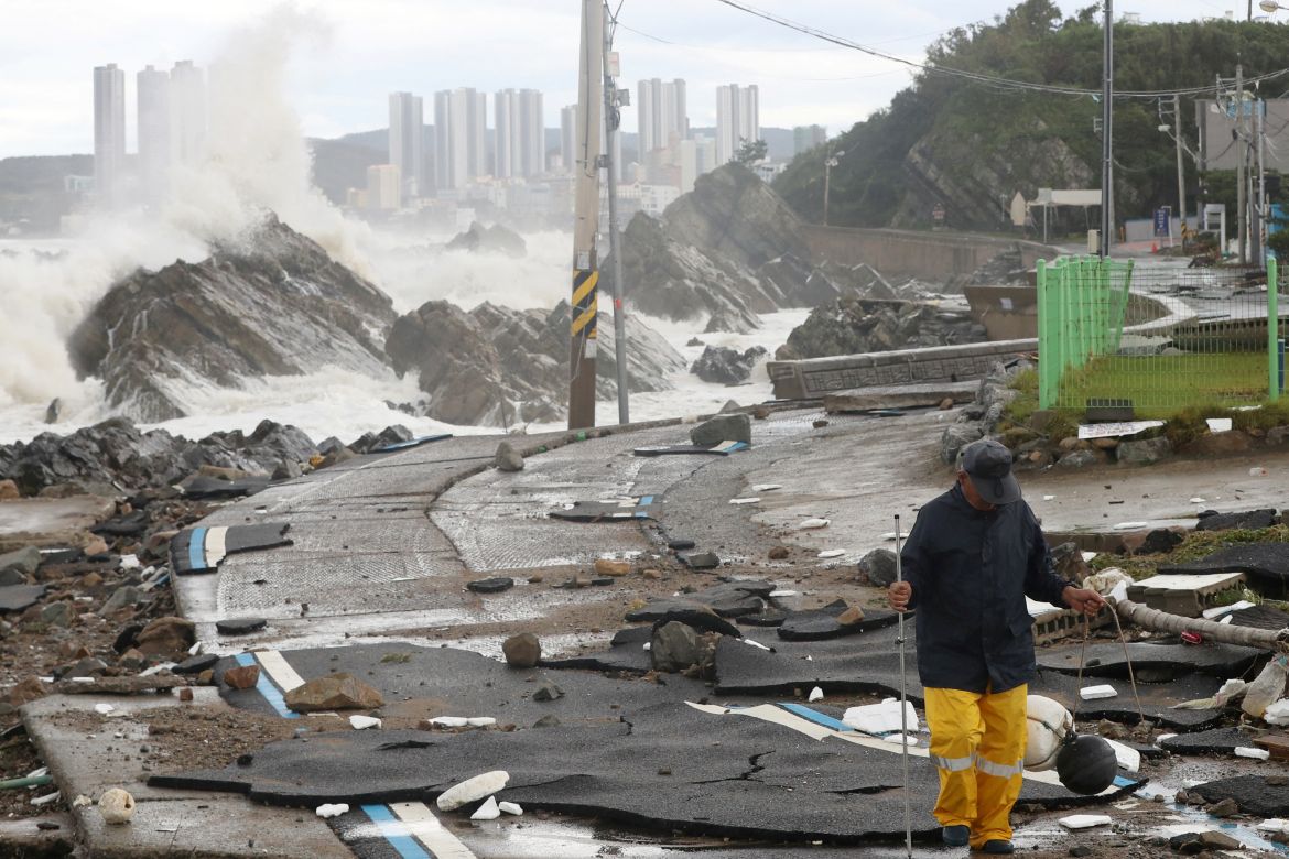 A man walks along a damaged coastal road