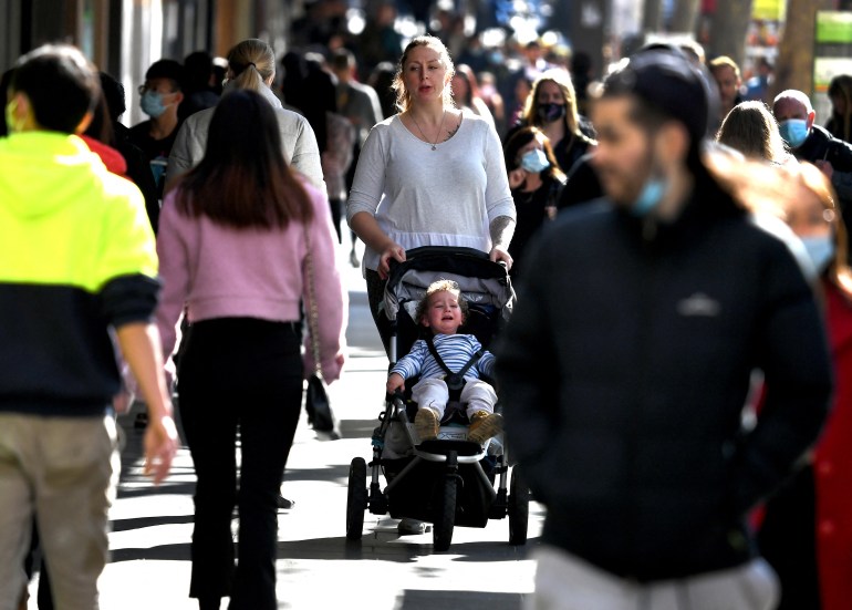 A woman pushes a push chair with her baby inside a crowded street in Melbourne
