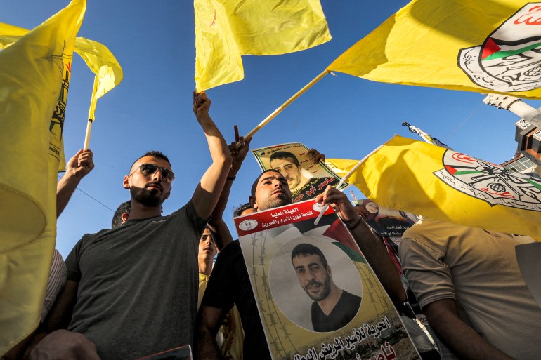 Protesters wave flags of Fatah and hold posters of Palestinian prisoner Nasser Abu Hamid during a demonstration in the centre of the city of Ramallah in the occupied West Bank on August 29, 2021 in support and demanding the release of Palestinian prisoners held in Israeli detention facilities.