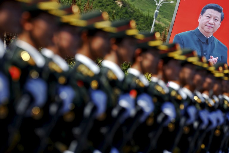 A Chinese military organization out of focus against a large banner with a photograph of Xi Jinping.