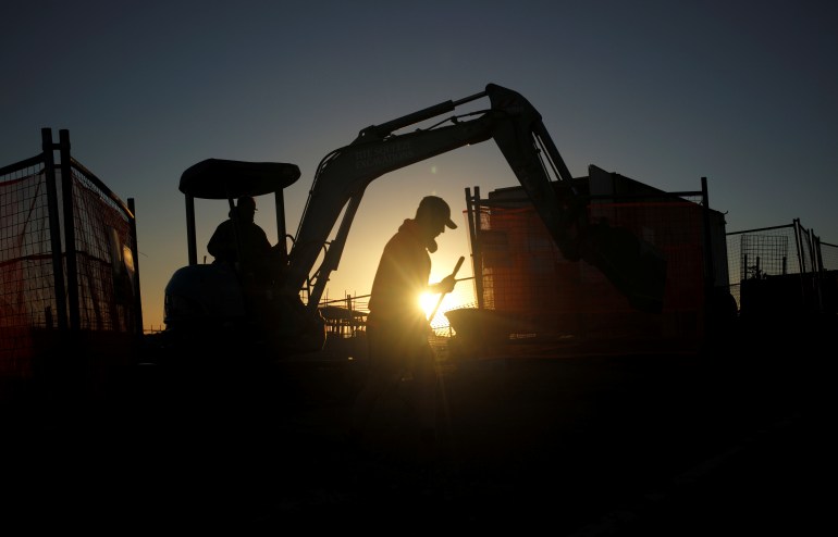 A worker on an excavator silhouetted against the sun.