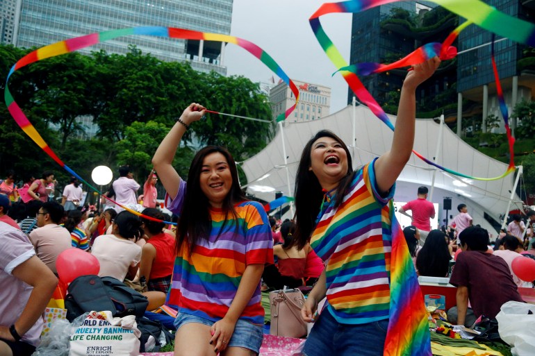 two women in rainbow flags and t-shirts wave rainbow banners at Pink Dot in Singapore