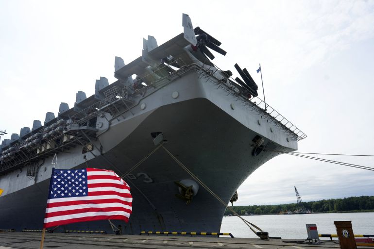 A United States flag flutters in front of a US Navy Wasp-class amphibious assault ship [File: Ints Kalnins/Reuters]