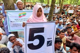 A Rohingya girl in a pink headscarf holds a sign with the number '5' as Rohingya gather to mark five years since they were driven out of Myanmar