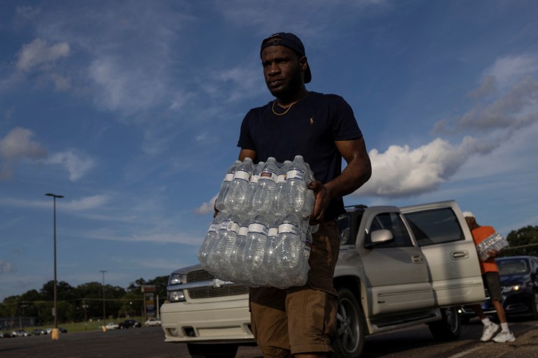 A volunteer carries bottles of water at a distribution site as the US city ...