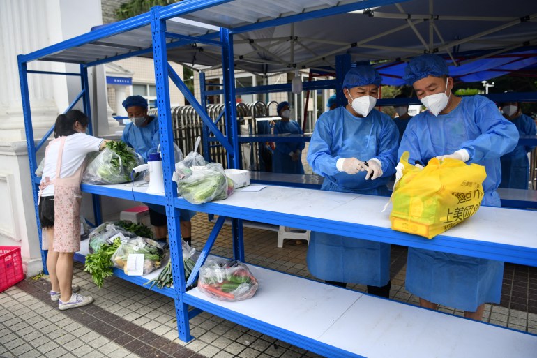 Workers in protective suits prepare to deliver food supplies placed on a rack outside a residential compound to its residents