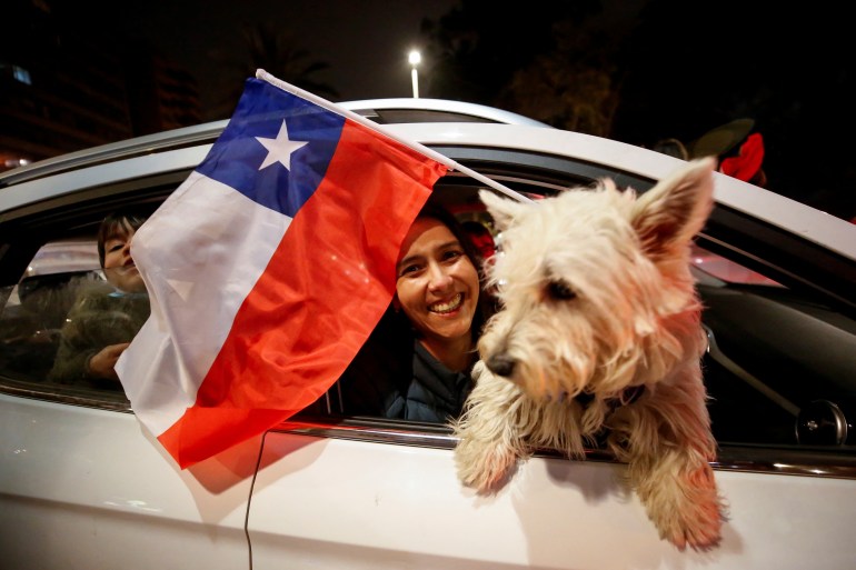 A reject supporter flies a Chile flag out of her car window with her dog looking out