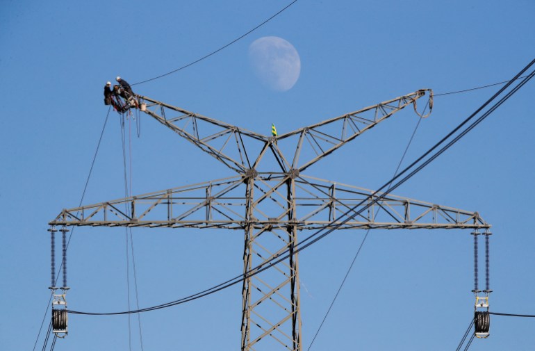 The moon rises as electricians work atop a power pole near the lignite power plant of Neurath of German energy supplier and utility RWE, near Rommerskirchen north-west of Cologne, Germany, February 5, 2020.