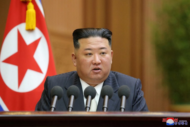 North Korean leader Kim Jong Un at a lectern with five microphones addressing the Supreme People's Assembly.