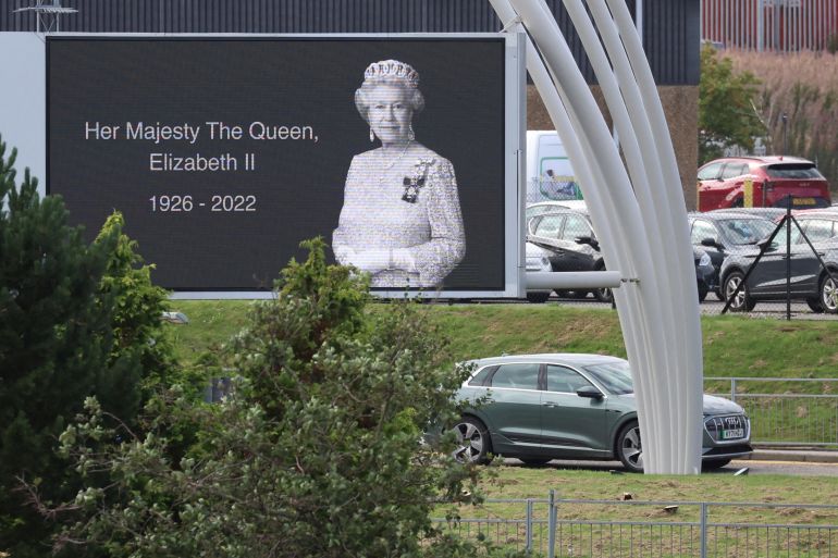 A car carrying Britain's King Charles and Queen Camilla drives past a poster of late Queen Elizabeth outside Aberdeen International Airport to fly to London, following the passing of Britain's Queen Elizabeth, in Aberdeen, Britain, September 9, 2022. REUTERS/Phil Noble