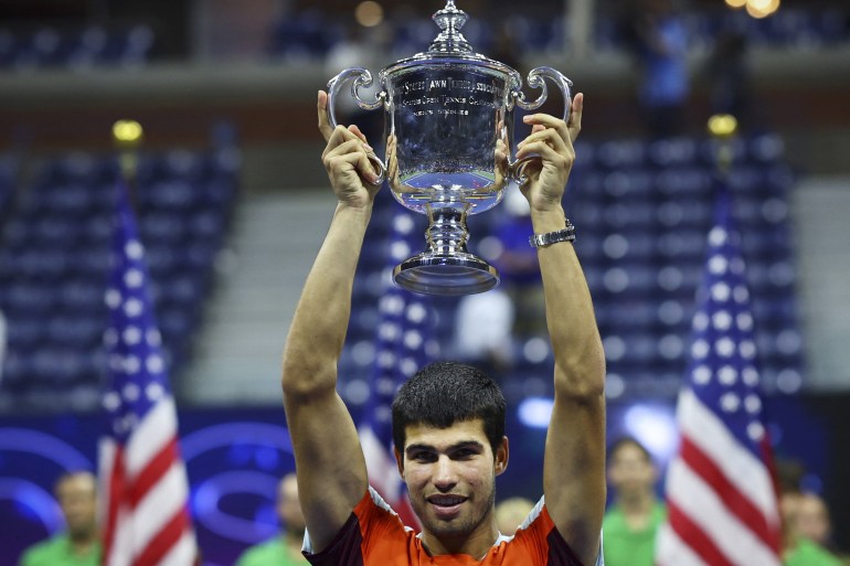 Spain's Carlos Alcaraz in a red jersey holds the US Open trophy aloft after winning the title