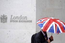 A worker shelters from the rain under a Union Flag umbrella as he passes the London Stock Exchange [File: Toby Melville/Reuters]