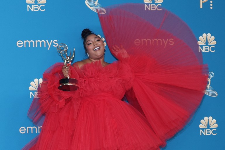 Lizzo, in a red dress, holds her Emmy