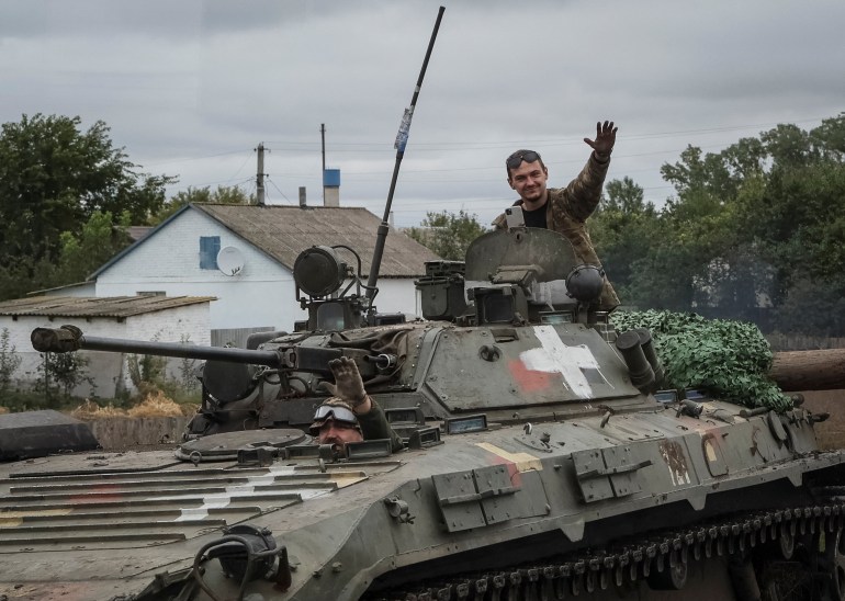 Two Ukrainian soldiers wave from their armored vehicle as they travel through a village liberated from Russian occupation.