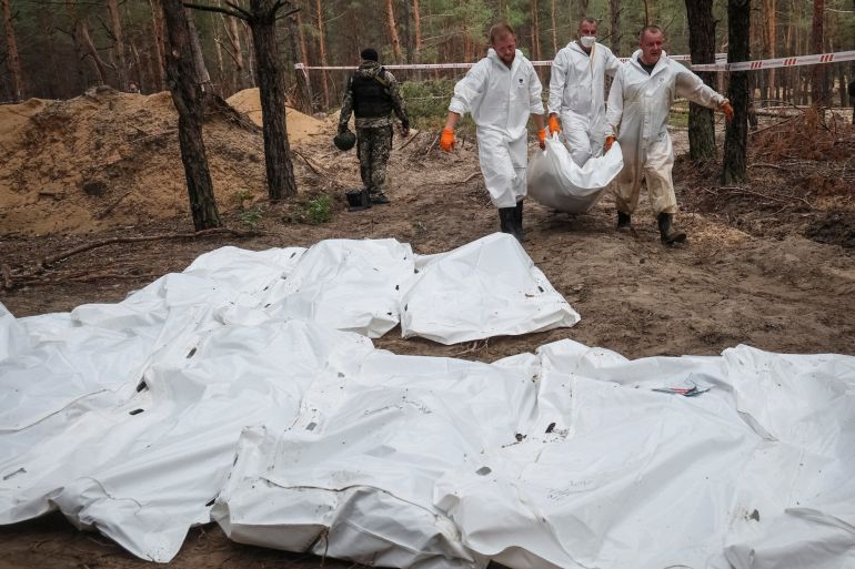 Experts carry a body as they work at a mass burial site in the town of Izium, recently liberated by Ukrainian Armed Forces, in Kharkiv region, Ukraine, on September 16, 2022 [Gleb Garanich/Reuters]