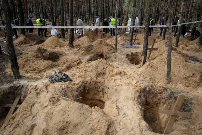 Police and experts work at a place of mass burial during an exhumation in Izium in Ukraine