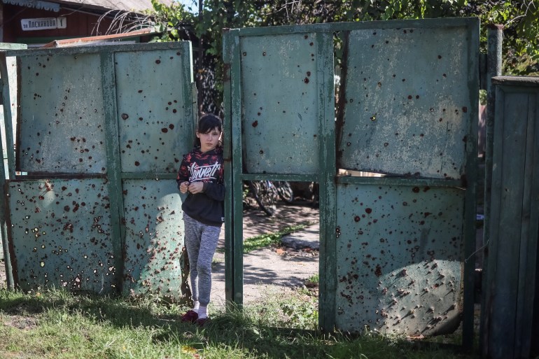 Uma menina ucraniana fica em um portão com buracos criados por estilhaços perto de sua casa, enquanto o ataque da Rússia à Ucrânia continua, na aldeia de Savyntsi, recentemente libertada pelas Forças Armadas Ucranianas, na região de Kharkiv, Ucrânia 21 de setembro de 2022. REUTERS/Gleb Garanich